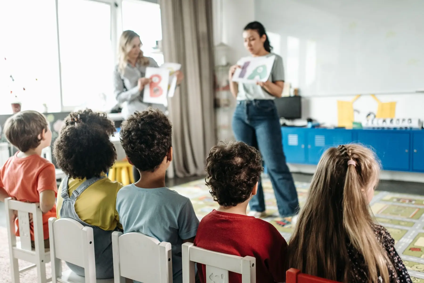 Un aula con chicos sentados escuchando a sus maestras